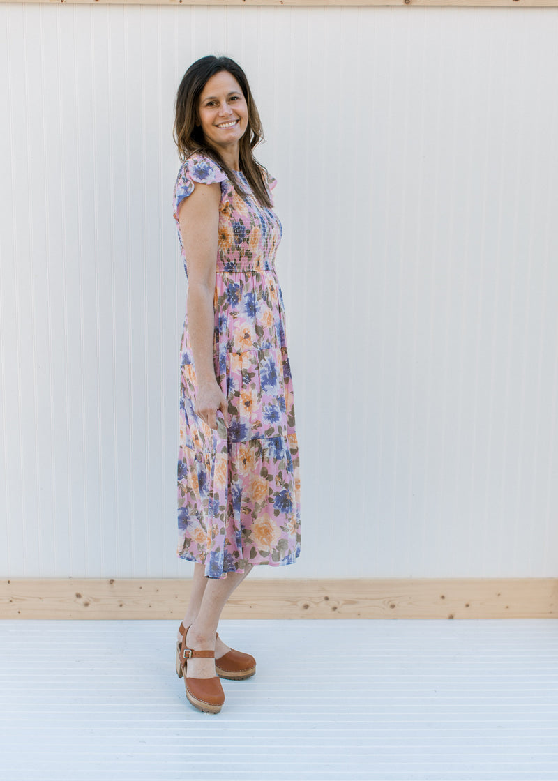 Model wearing heels with a lilac dress with purple, peach and green floral and a smocked bodice.