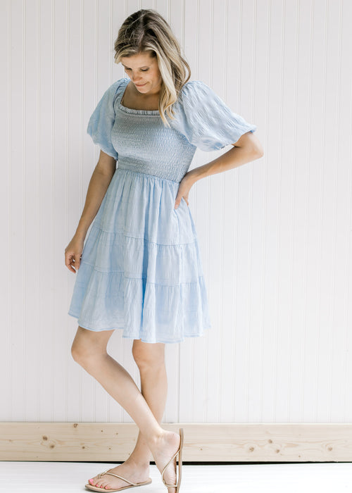 Model wearing a baby blue dress with a smocked bodice, square neckline and sandals. 