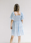 Back view of Model wearing a baby blue dress with a smocked bodice, square neckline and sandals. 