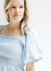 Close up view of a smocked bodice and short bubble sleeves on a model warning a baby blue dress.