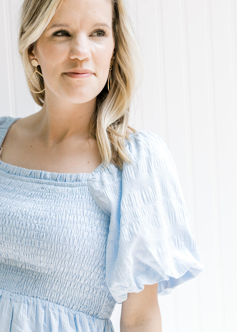 Close up view of a smocked bodice and short bubble sleeves on a model warning a baby blue dress.
