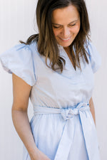 Close up of puff short sleeves, v-neck and a tie at the waist of a baby blue midi. 