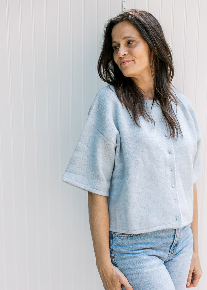 Model wearing a baby blue knit sweater with short sleeves, buttons and a slightly cropped fit.