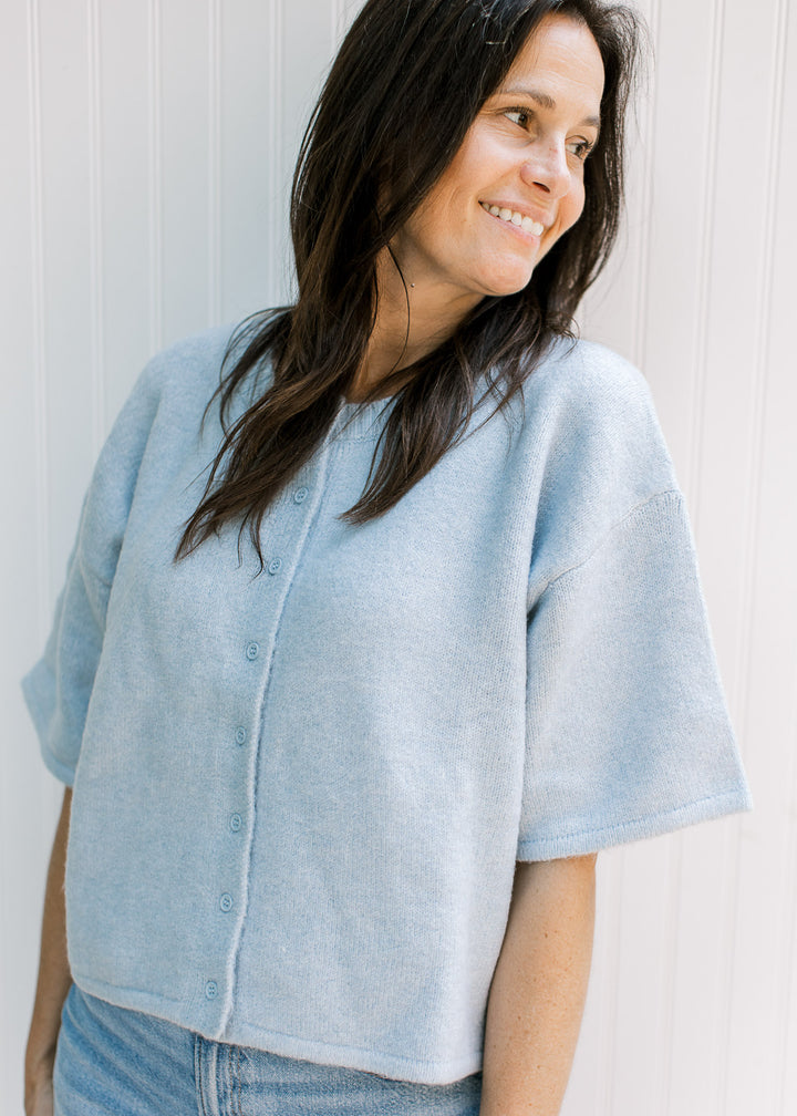 Model wearing a baby blue knit sweater with short sleeves, buttons and ribbed neck, hem and cuff.