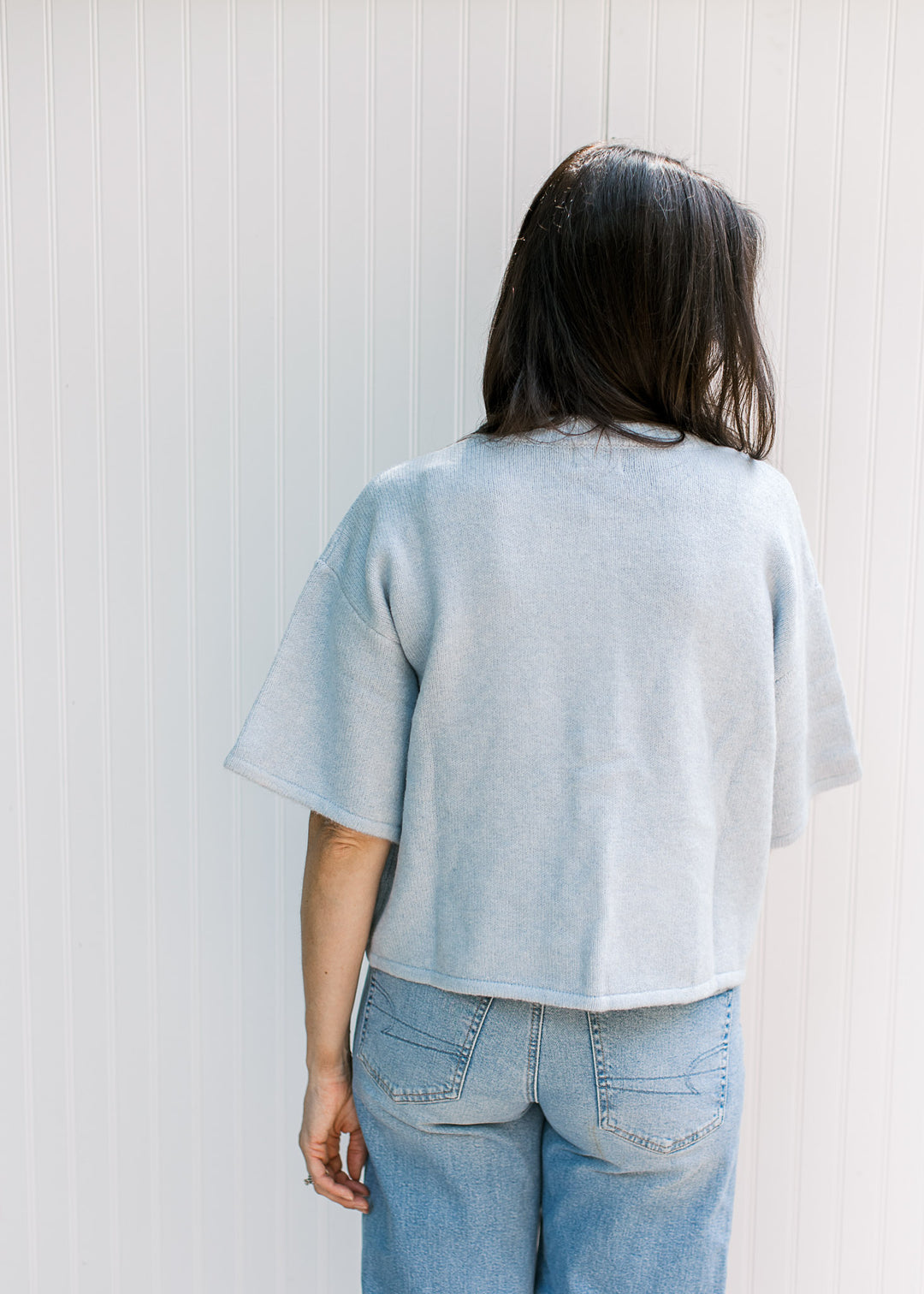 Back view of Model wearing a baby blue knit sweater with short sleeves and buttons. 