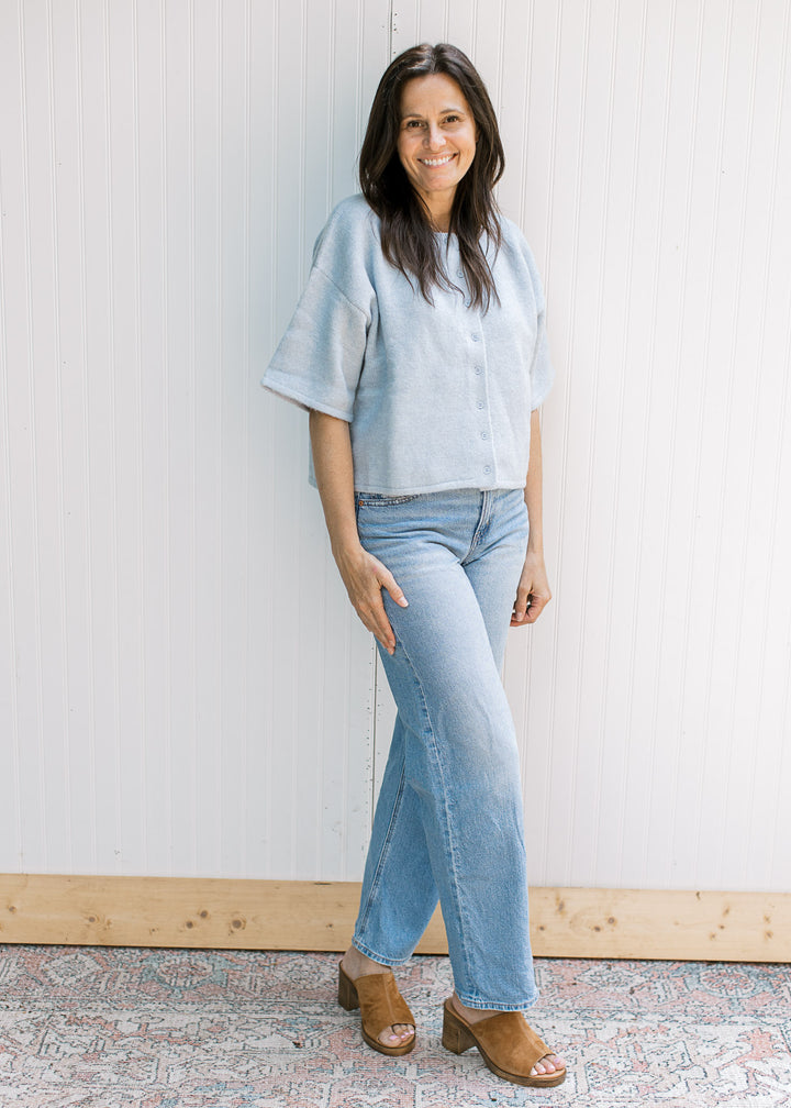 Model wearing jeans with a baby blue knit sweater with short sleeves and buttons. 