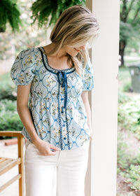 Model wearing a baby blue babydoll top with faux buttons and tie, scoop neck and short sleeves.