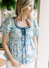 Model wearing a baby blue top with faux buttons and tie, scoop neck and bubble short sleeves.