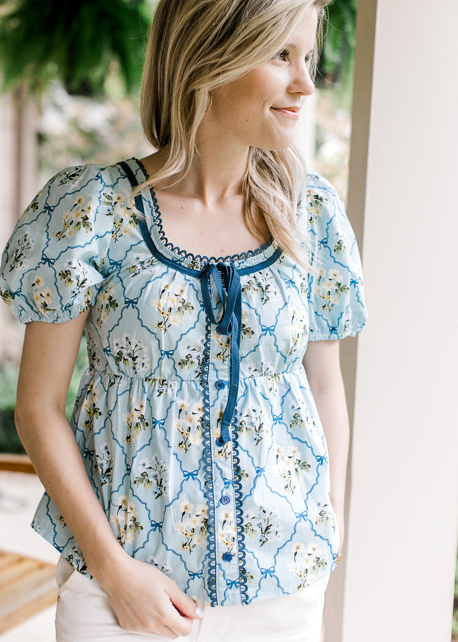 Model wearing a baby blue top with faux buttons and tie, scoop neck and bubble short sleeves.