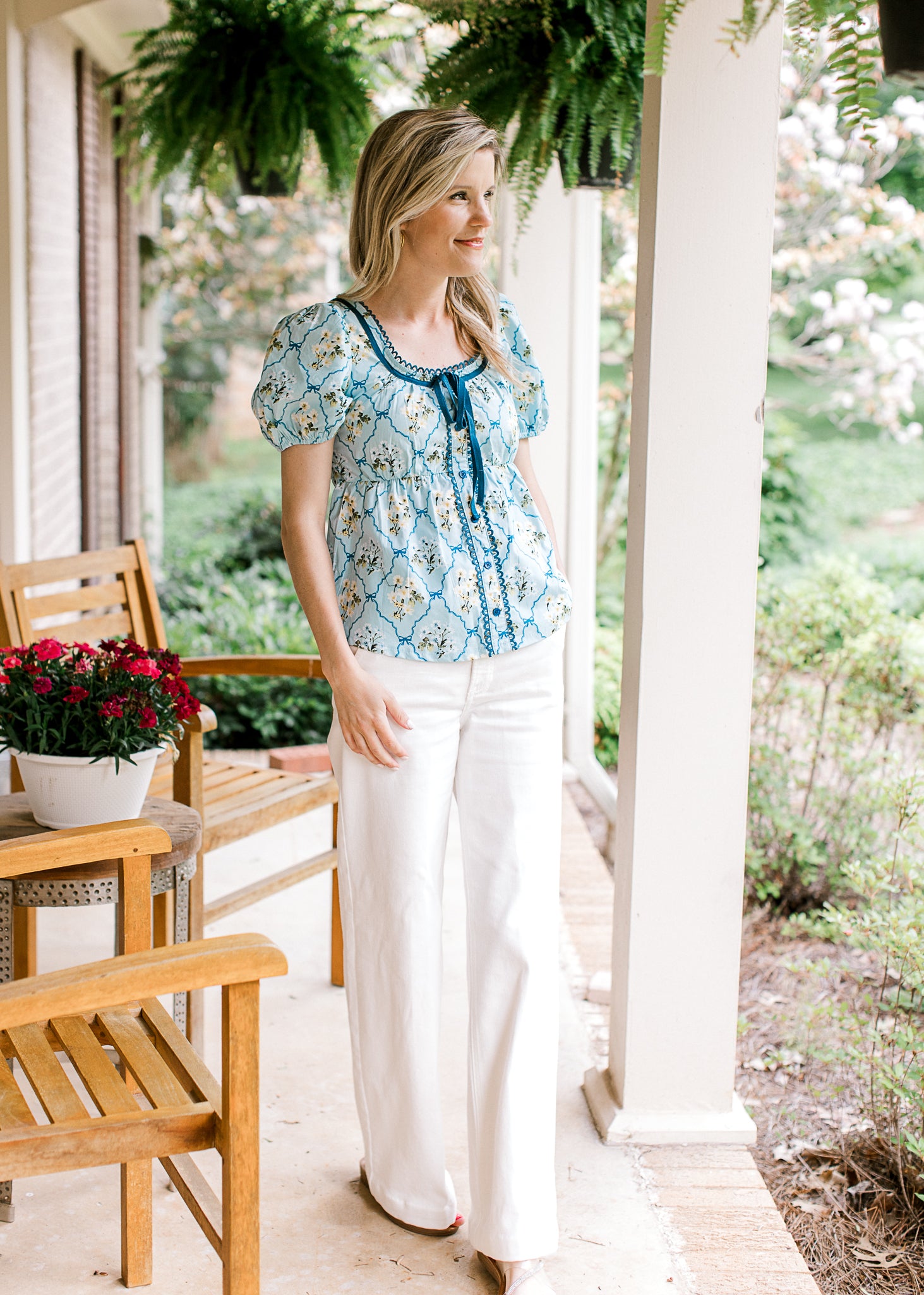 Model wearing white pants and a baby blue top with faux buttons, scoop neck and short sleeves.