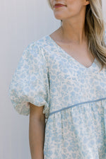 Close up of bubble short sleeves and v-neck on a cream dress with blue flowers. 