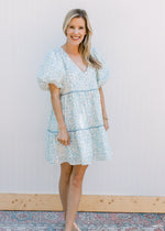 Model wearing a cream above the knee dress with blue flowers, v-neck and bubble short sleeves.