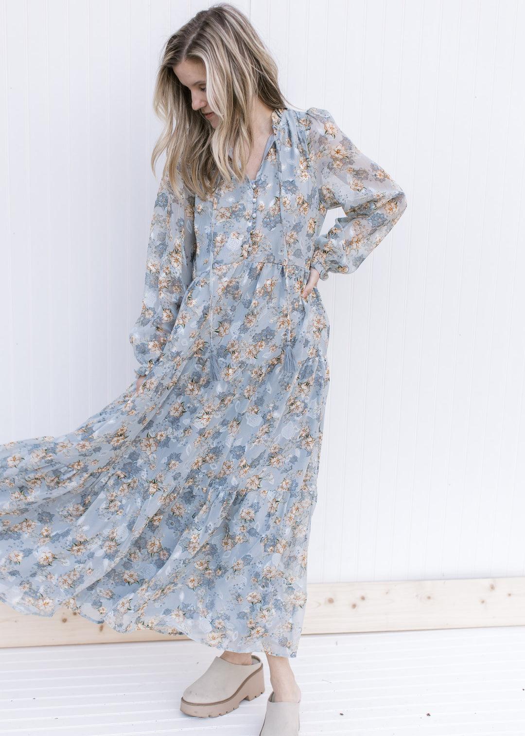 Model wearing a lined pale blue maxi with gold, cream and ivory floral and long sheer sleeves.