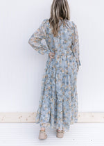 Back view of Model wearing a pale blue maxi with gold, cream and ivory floral and long sheer sleeves