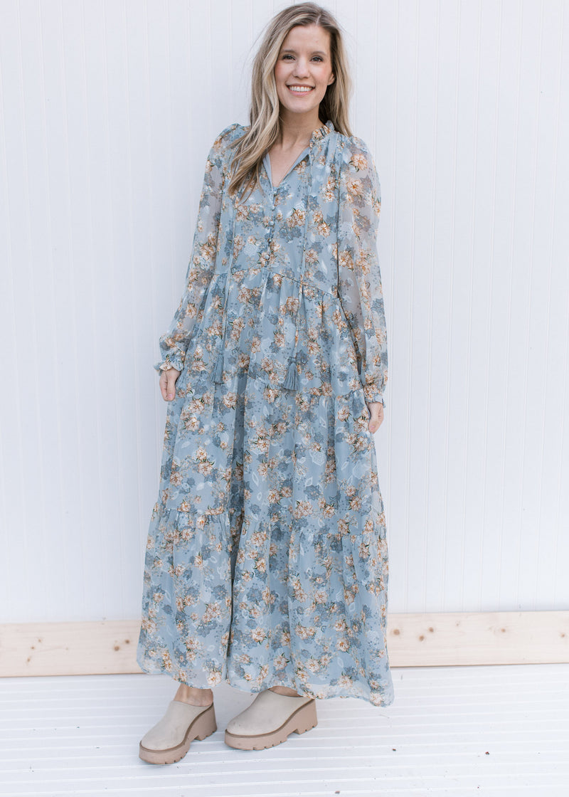 Model wearing mules and a pale blue maxi with gold, cream and ivory floral pattern and long sleeves.