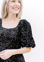 Close up of square neck, elastic waist and 3/4 sleeves on a black sequins above the knee dress. 