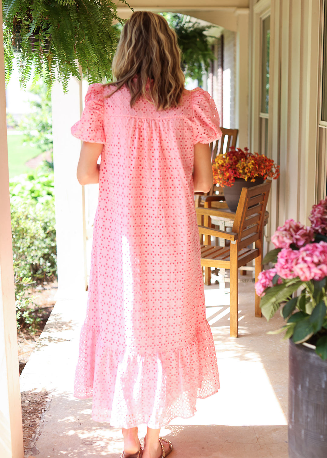 Back view of Model wearing a pink midi with eyelet detail, short bubble sleeves and ruffle hem.