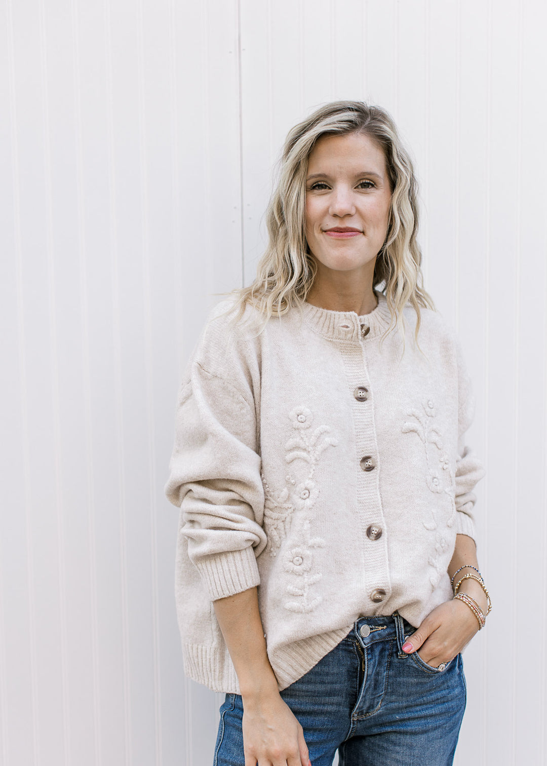 Model wearing a cream long sleeve cardigan with tone-on-tone 3D floral detail.