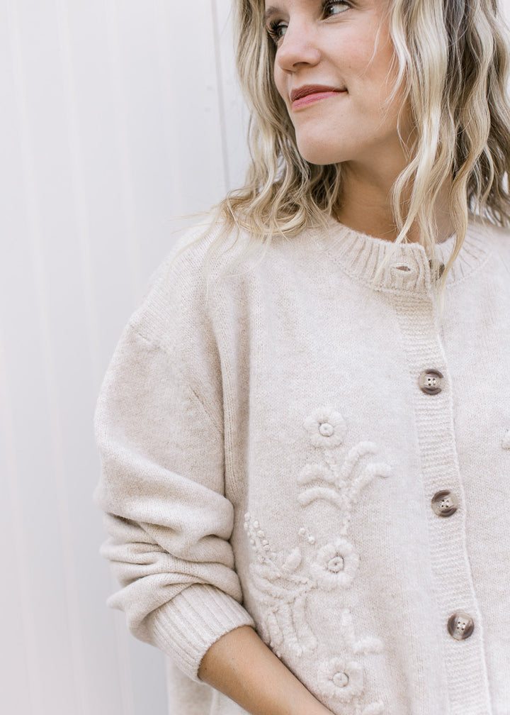 Close up of 3D floral and brown buttons on a cream long sleeve cardigan with ribbed details.