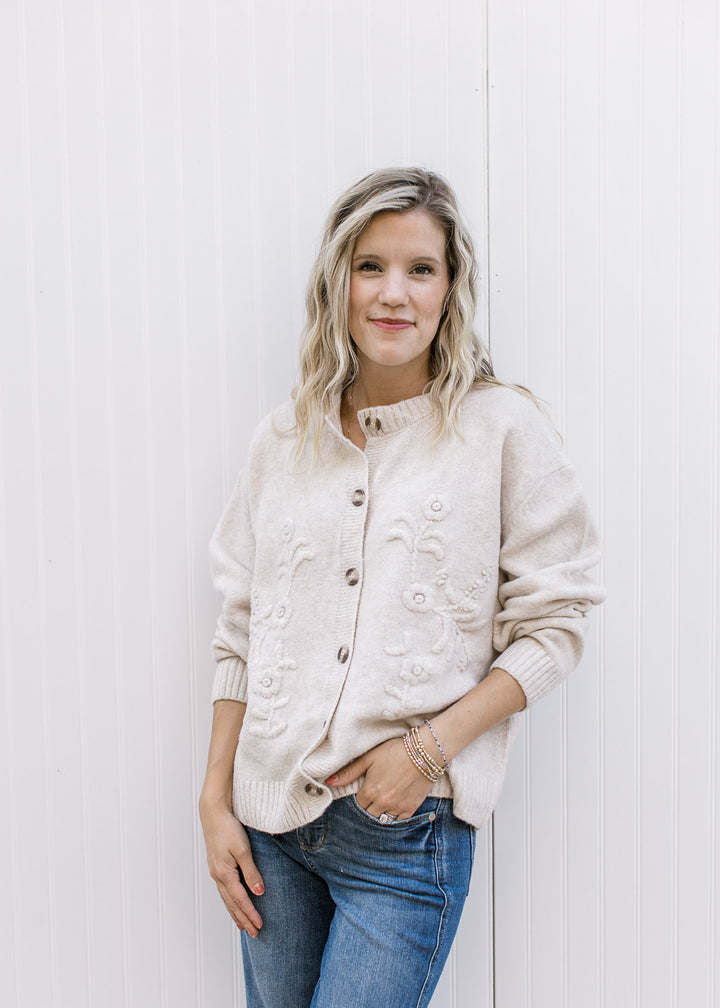 Model wearing jeans and a cream long sleeve cardigan with tone-on-tone 3D floral detail.