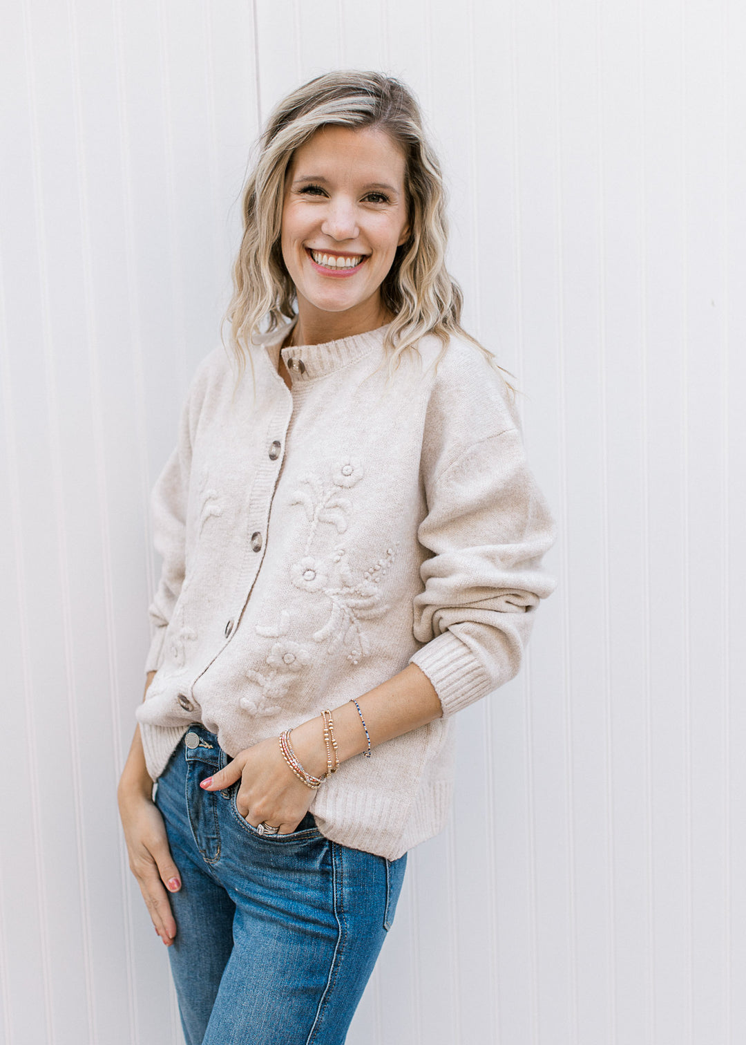 Model wearing a cream long sleeve, button-up cardigan with tone-on-tone 3D floral detail.