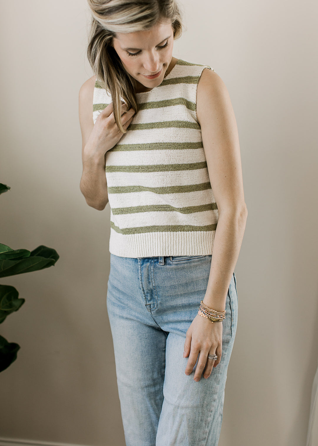 Model wearing a sleeveless and sage striped knit with a round neck and ribbed hem. 