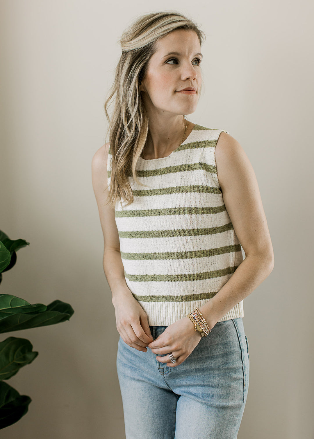 Model wearing a sleeveless cream top with sage stripes, round neck and open back with tie closure.