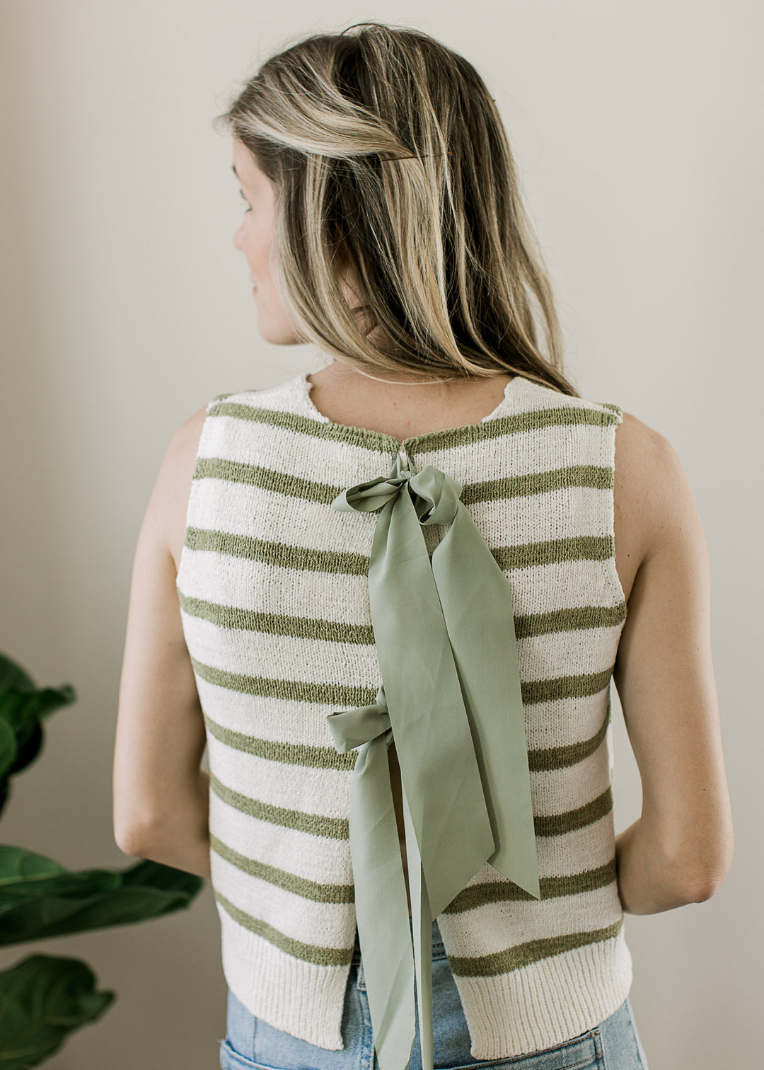 Close up of sage ribbon tie closure on the back of a sleeveless cream top with sage stripes. 
