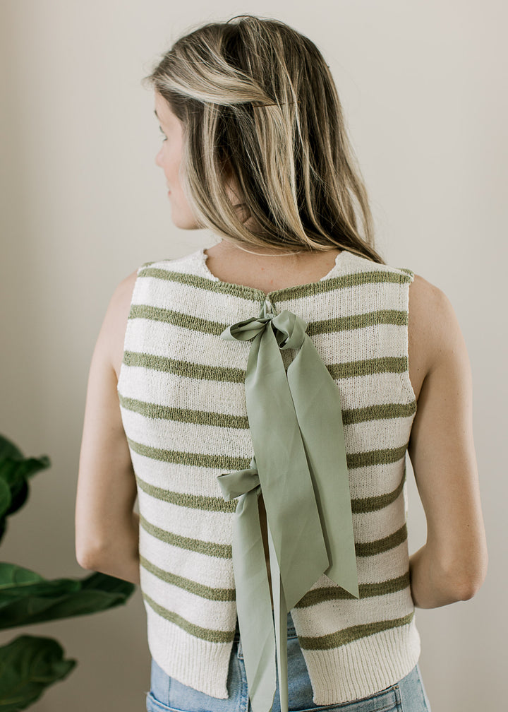 Close up of sage ribbon tie closure on the back of a sleeveless cream top with sage stripes. 