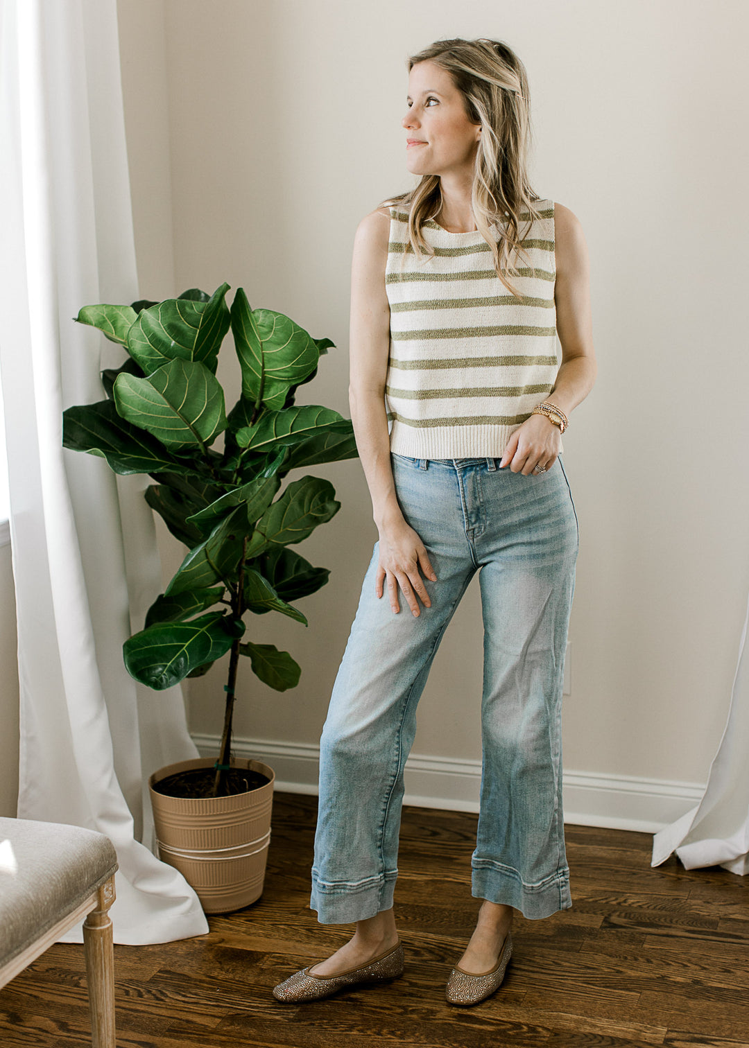 Model wearing jeans and a sleeveless cream top with sage stripes, round neck and tie back closure.