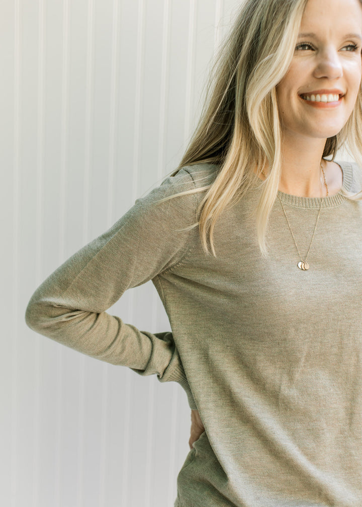 Model wearing an olive long sleeve sweater with a round neck and a lightweight material. 