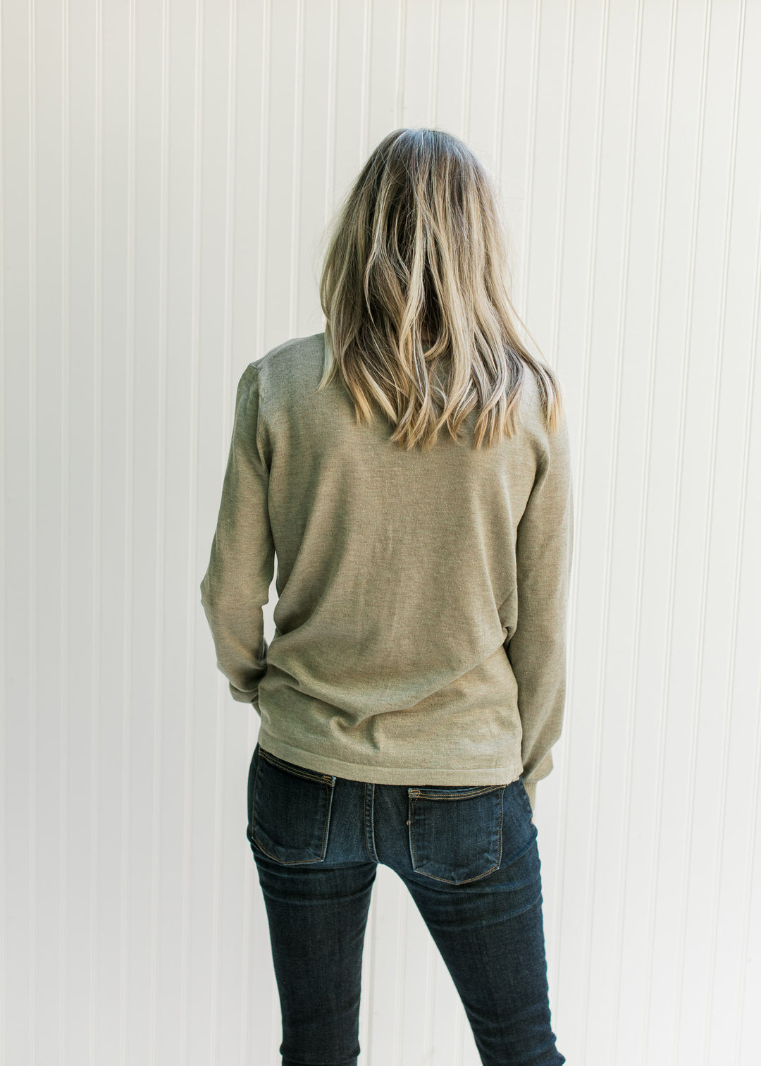 Back view of a Model wearing an olive long sleeve sweater with a round neck and a light material. 