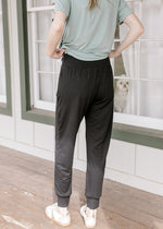 Back view of model wearing black joggers with curved seam on bottom and elastic wasitband.