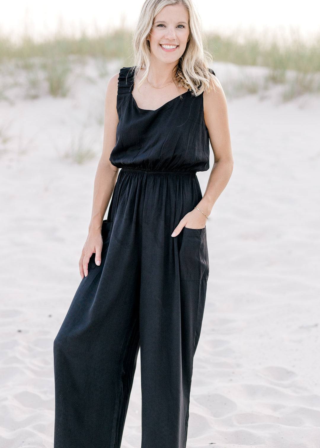 Model wearing a black wide leg jumpsuit with side patch pockets and elastic waist. 