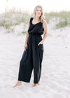 Model wearing a v-neck  black wide leg jumpsuit with side patch pockets and elastic waist.