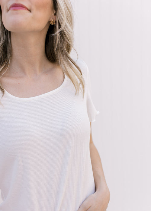Model wearing a cream ribbed top with ruffled at hem and short sleeve. 