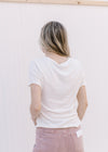 Back view of Model wearing a cream ribbed top with ruffled at hem and short sleeve.
