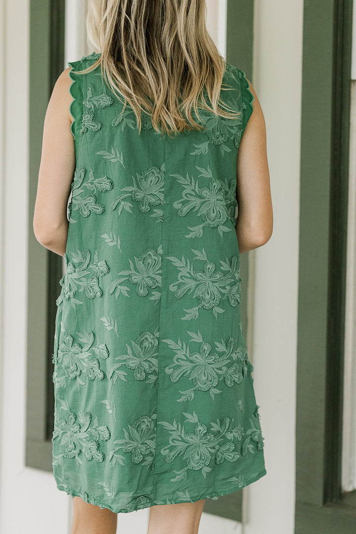 Back view of Model wearing a green tone on tone textured sleeveless dress with pockets. 
