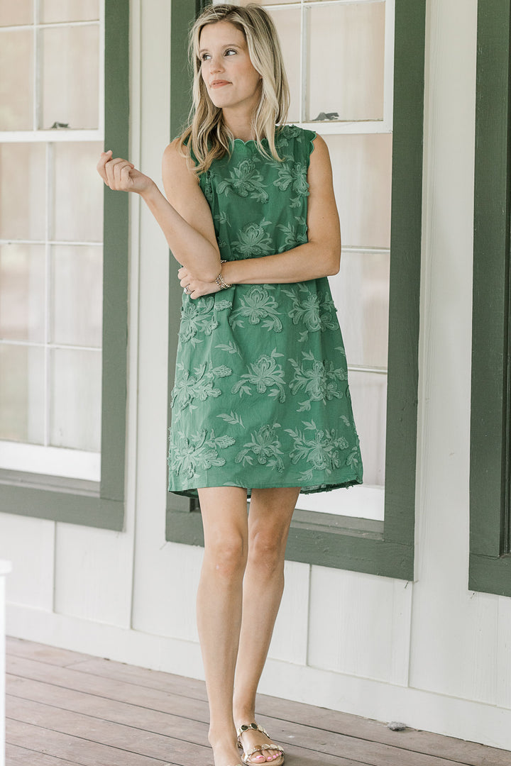 Model wearing sandals with a green tone on tone textured sleeveless dress with pockets. 