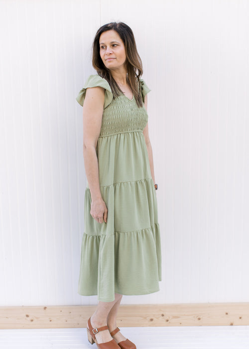 Model wearing a basil green tiered midi with a smocked bodice and ruffle capped sleeves.
