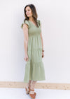 Model wearing heels with a basil green tiered midi with a smocked bodice and ruffle capped sleeves.