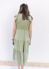 Back view of Model wearing a basil green midi with a smocked bodice and ruffle capped sleeves.