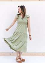 Model twirling in a basil green tiered midi with a smocked bodice and ruffle capped sleeves.