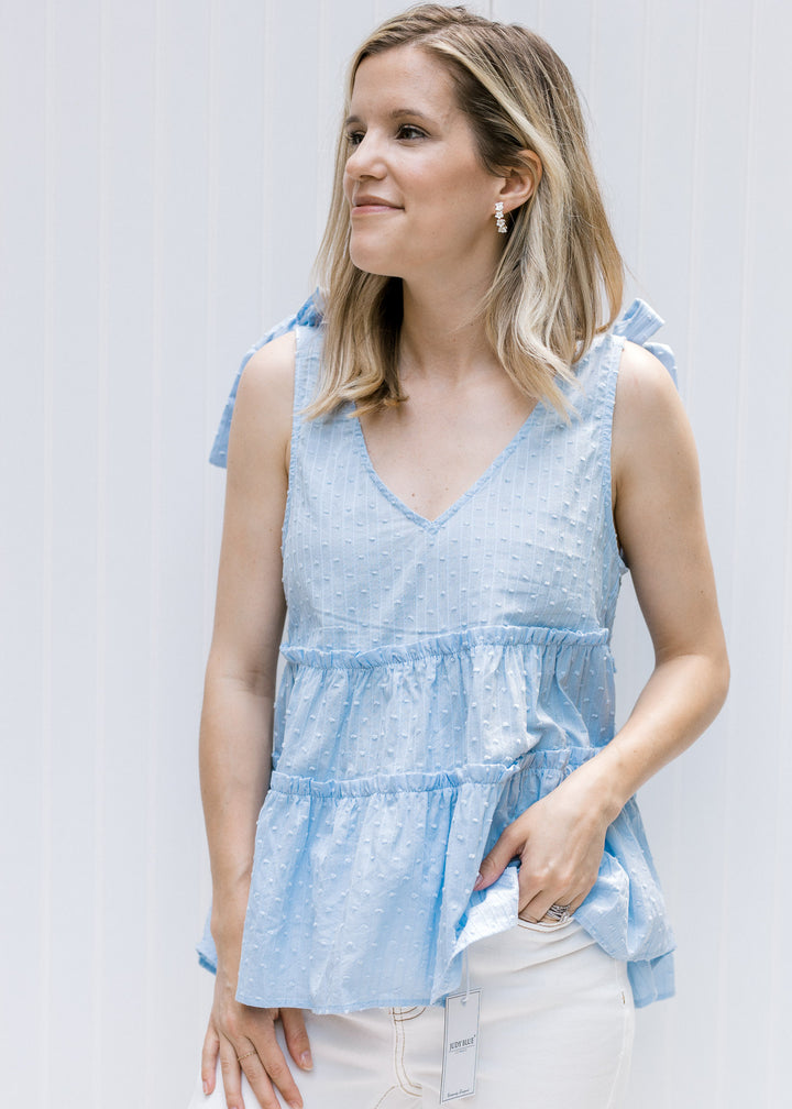 Model wearing white jeans with a pale blue v-neck top with dotted Swiss fabric and ruffled tiers.