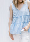 Close up view of tiers and dotted Swiss fabric on a pale blue sleeveless top with ties at shoulder. 