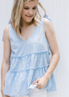 Model wearing a pale blue v-neck top with dotted Swiss fabric, ruffled tiers and a true shoulder tie