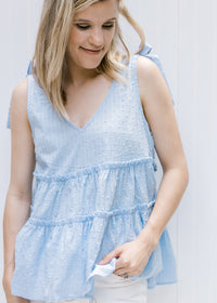 Model wearing a pale blue v-neck top with dotted Swiss fabric, ruffled tiers and a true shoulder tie