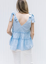 Back view of Model wearing a pale blue v-neck top with dotted Swiss fabric and ruffled tiers.