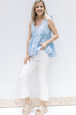 Model wearing white jeans and wedges with a pale blue v-neck top with dotted Swiss fabric. 