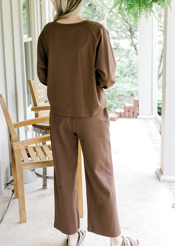 Back view of Model wearing a mocha colored set, top has long sleeves and with wide leg bottoms. 